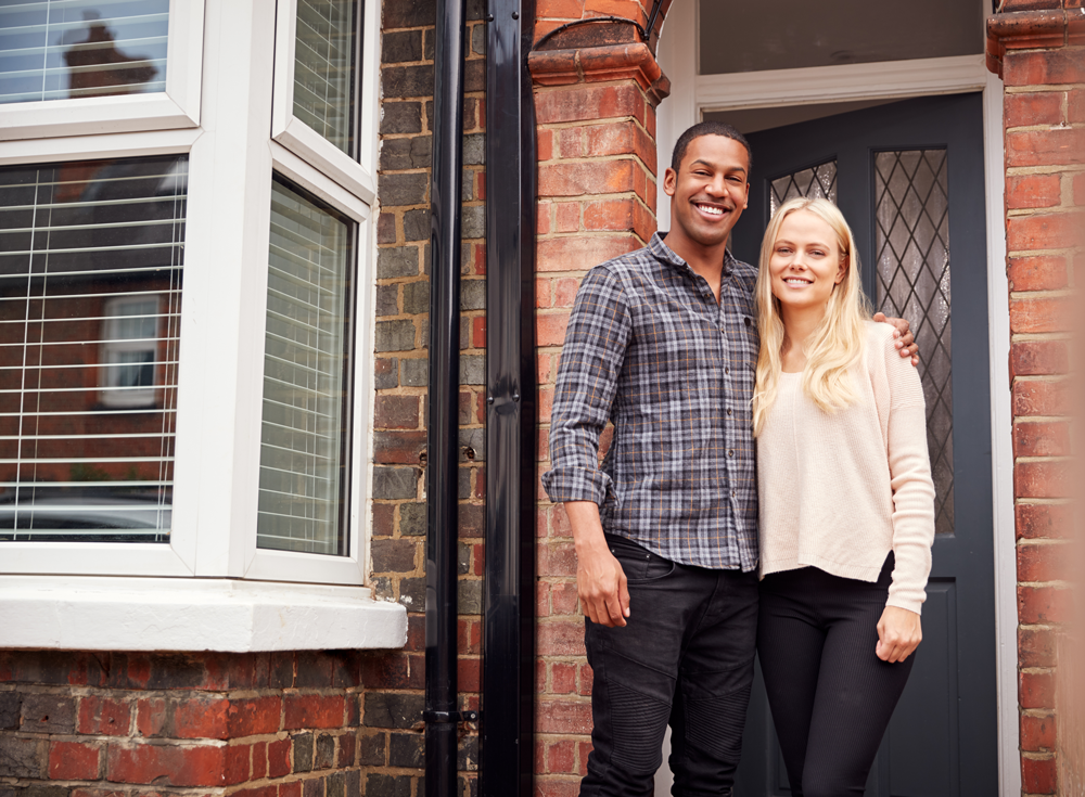 couple smiles for the camera in front of their home