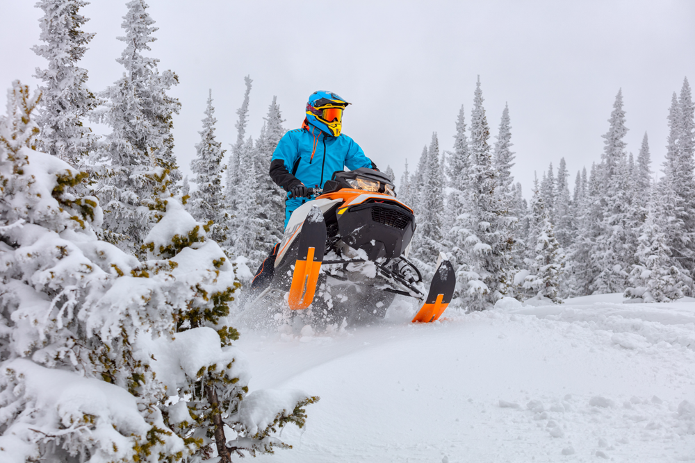 person rides an orange snowmobile surrounded by snow-covered trees