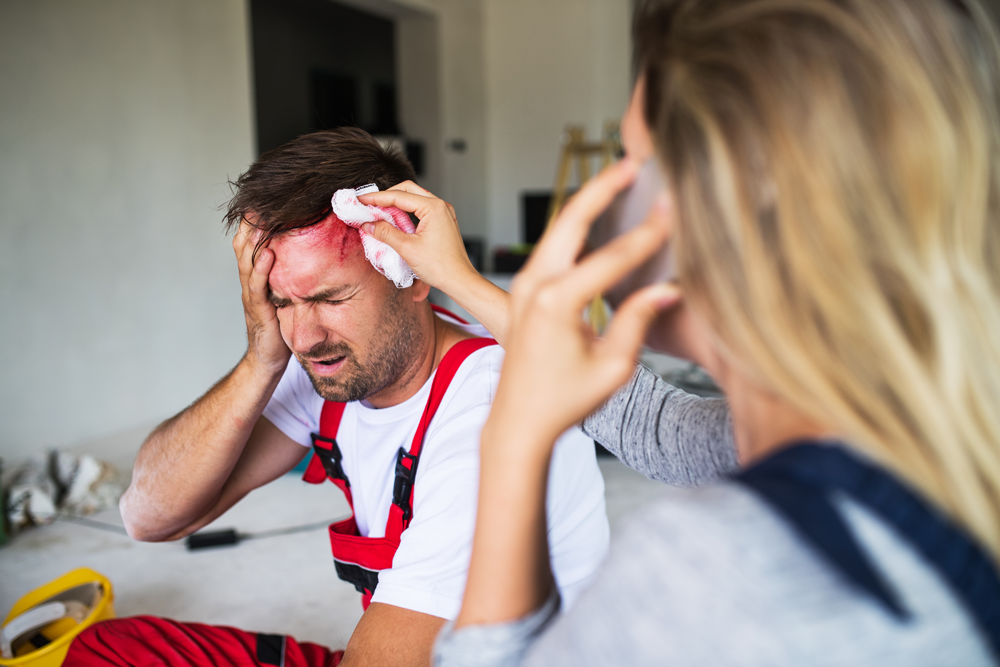 Person with head wound holds head while onlooker dabs wound