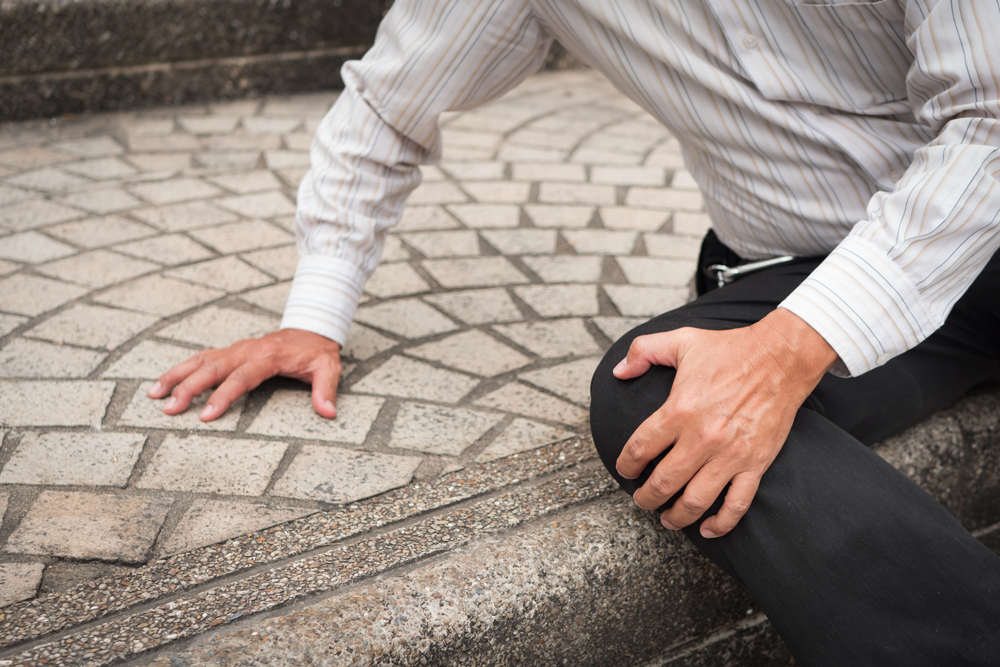 Person sits on sidewalk grasping knee